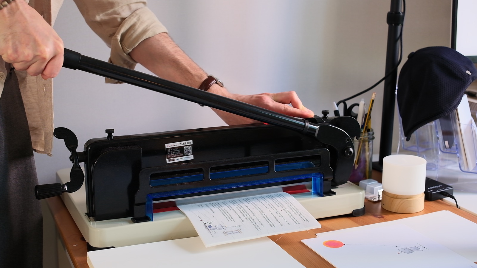 Jordan Monnet pulling the lever of a guillotine paper cutter, a blue alignment guide set against the blade